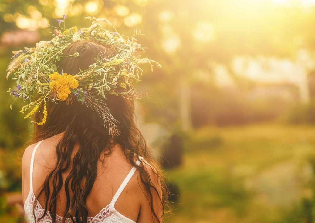 Ansicht einer Frau mit Blütenkranz auf dem Kopf, in Sommerkleid, steht auf einer Wiese